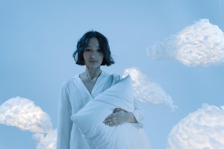 Woman In White Pajamas Holding A Pillow Near The Clouds