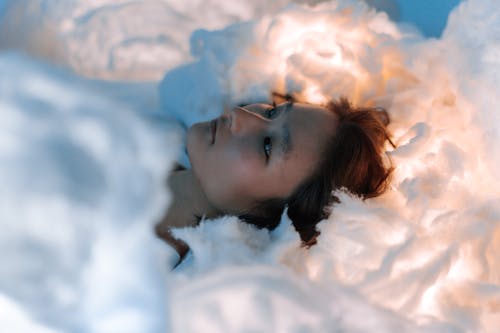 A Woman in White Long Sleeves Lying on a White Textile