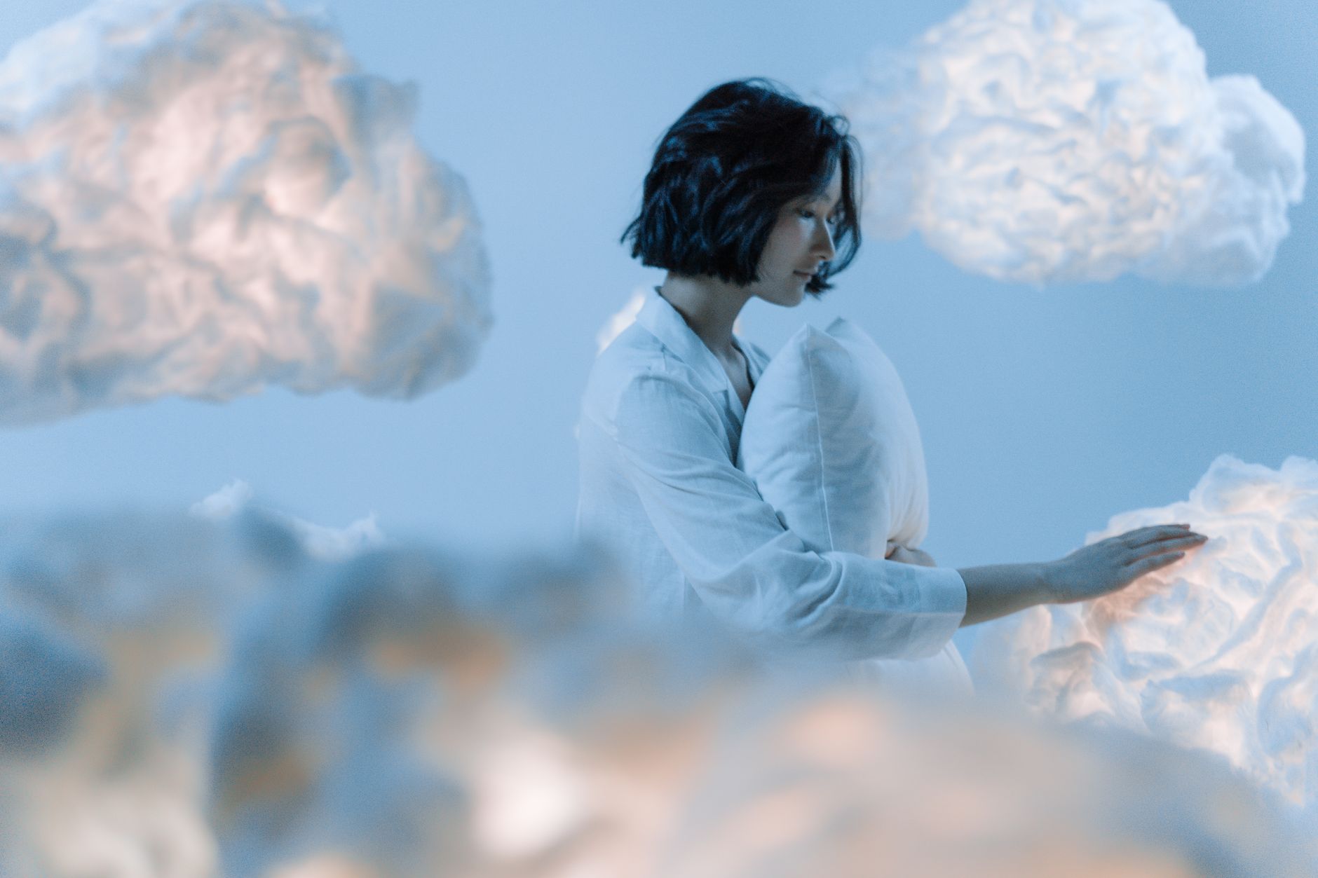 A serene scene of an Asian woman dreaming among soft, ethereal clouds.