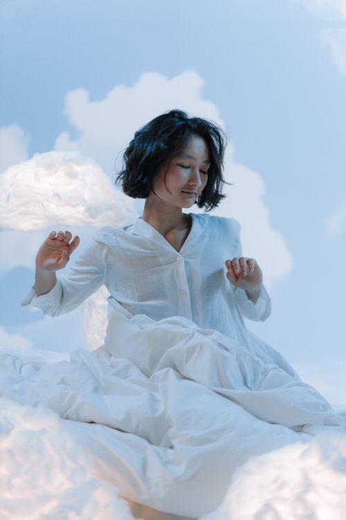 Free A serene woman in white surrounded by clouds, conveying a dreamy and peaceful atmosphere. Stock Photo
