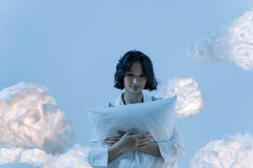 Free A serene scene of a woman in white surrounded by ethereal clouds, embracing a pillow. Stock Photo