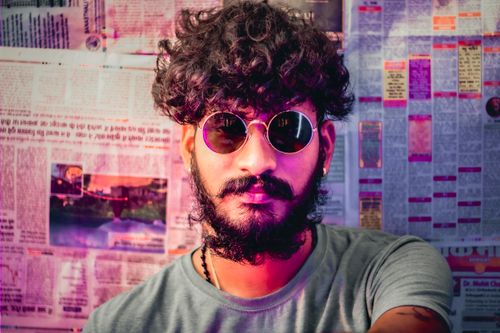 Free Stylish man with curly hair and beard wearing sunglasses against a newspaper background. Stock Photo