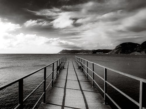 A Grayscale Photo of a Boardwalk Near the Ocean