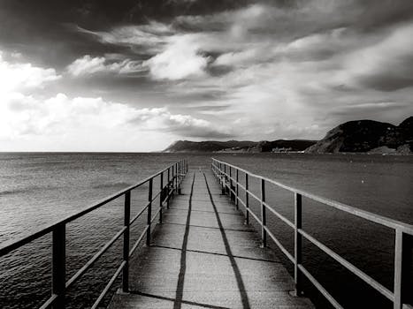 Black and white photo of a pier extending into the ocean under a dramatic sky.