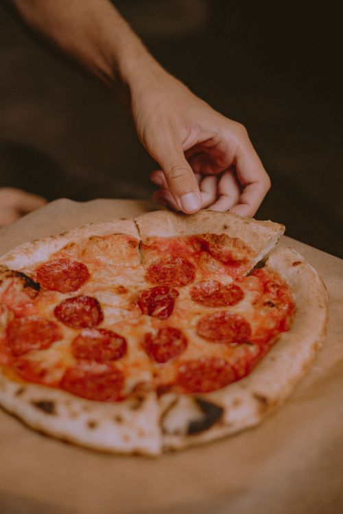 Free Close-up of a hand holding a slice of delicious pepperoni pizza on a brown paper. Stock Photo