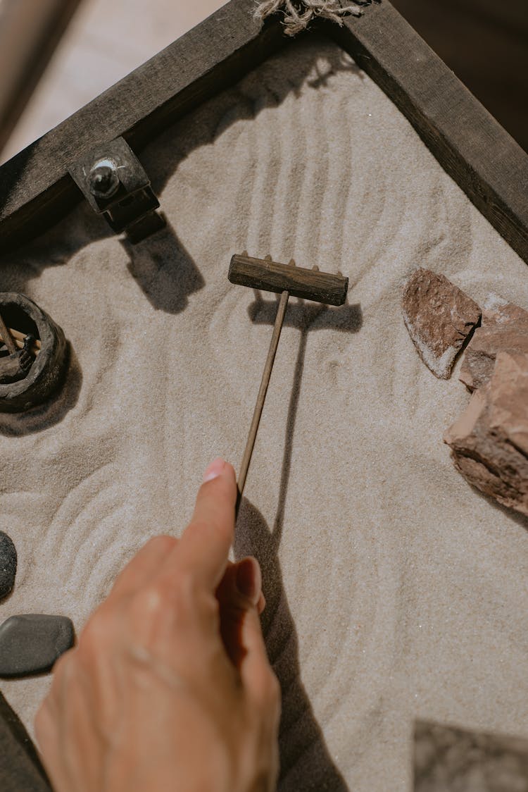 Hand With Rake Over Sand In Frame