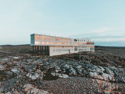 Free A striking modern building perched on rocky terrain under a pastel sky at sunset. Stock Photo