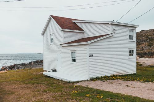 Free Charming white coastal house with red roof near rocky seashore on a cloudy day. Stock Photo