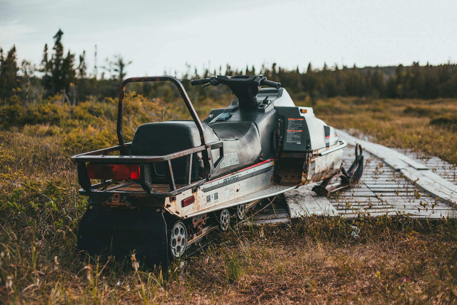 An old, rusty Yamaha snowmobile parked on a grassy trail, surrounded by nature.