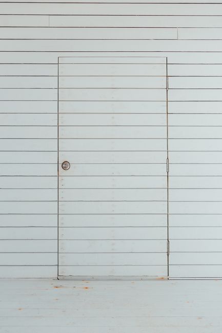 A minimalist photo of a white wooden door seamlessly blending into a panel wall, emphasizing simplicity and design.