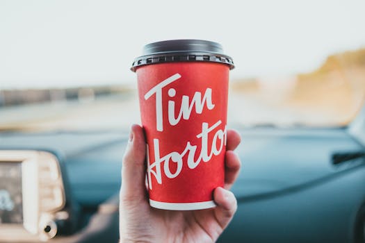Person holding a red Tim Hortons coffee cup inside a car, suggesting a takeaway beverage.