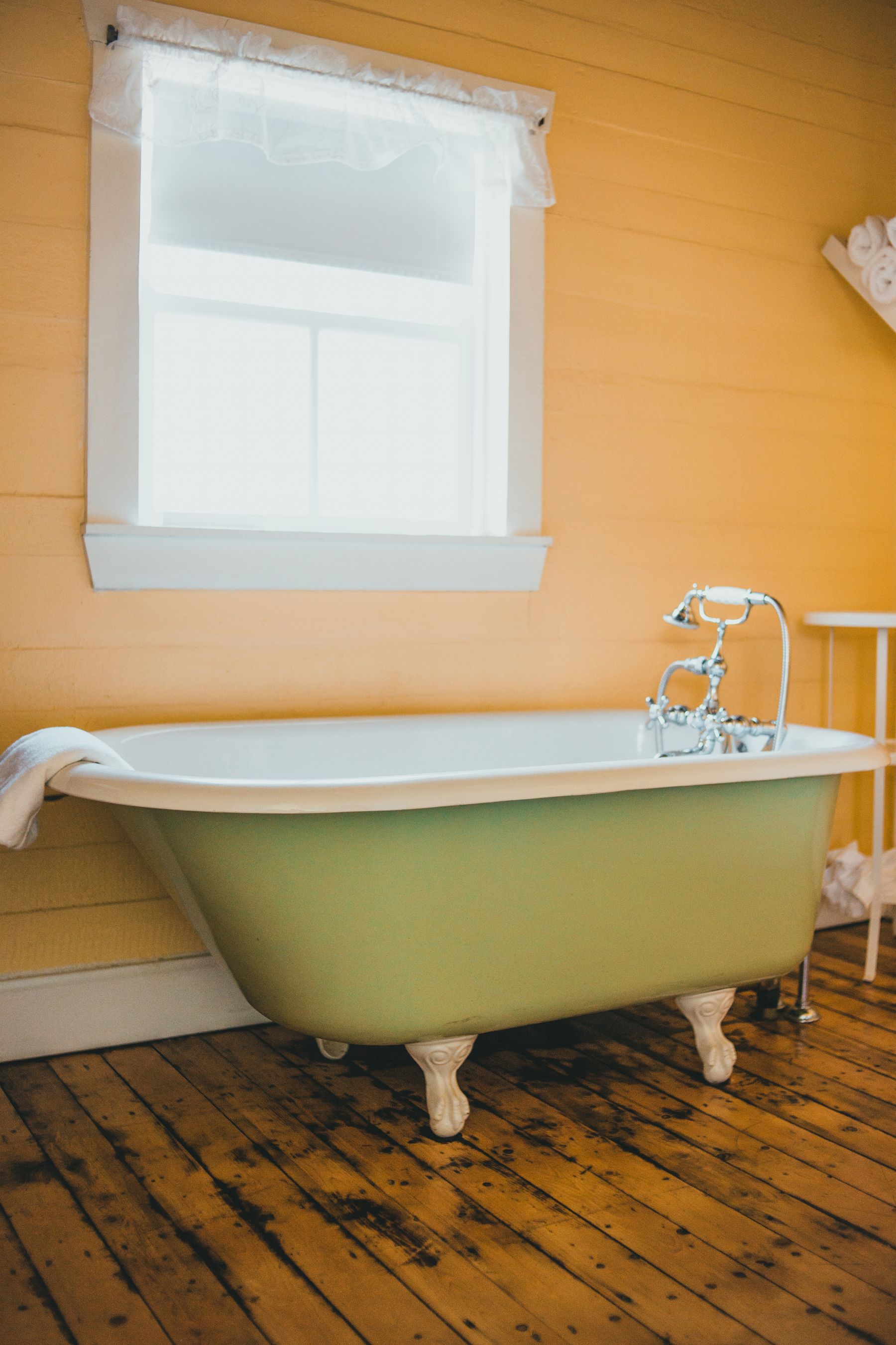 Old-fashioned deep green clawfoot bathtub with brass faucet and warm wood floor