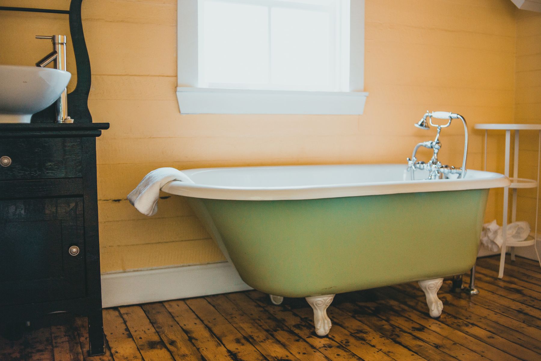 Classic clawfoot bathtub beside warm wood floor and window