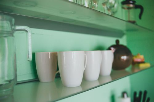 Free Close-up photo of a minimalist kitchen shelf featuring white mugs and glass kitchenware. Stock Photo