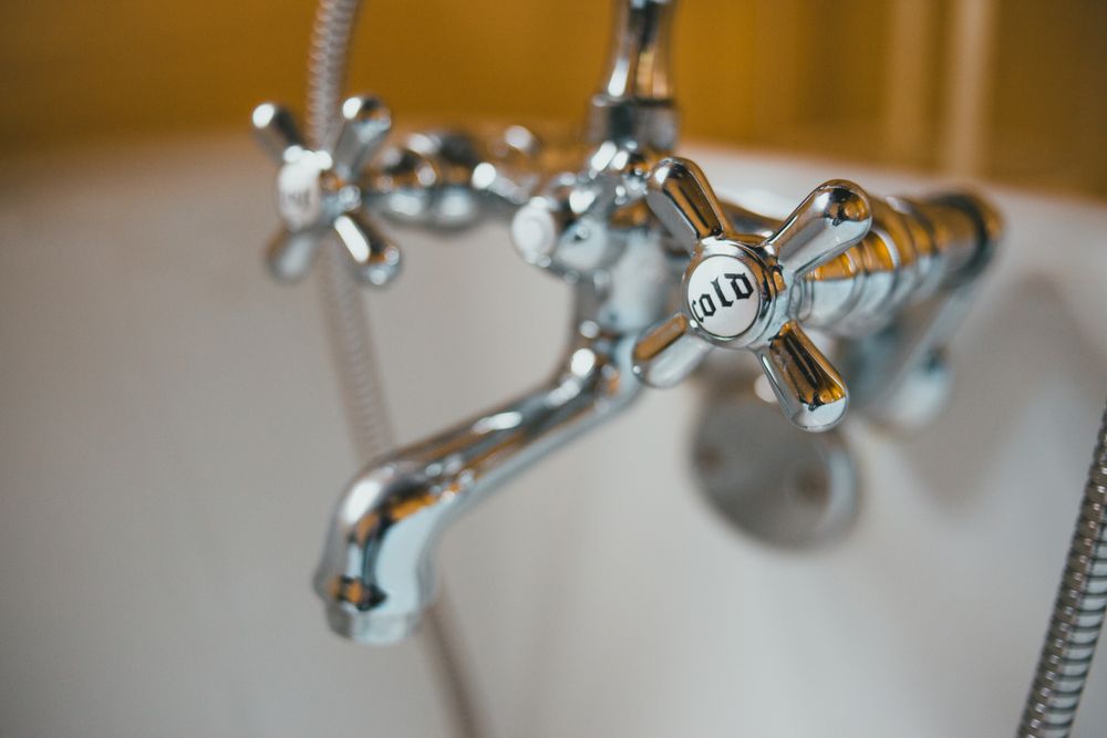 Chrome bath tap with a cold-water cross handle over a white tub