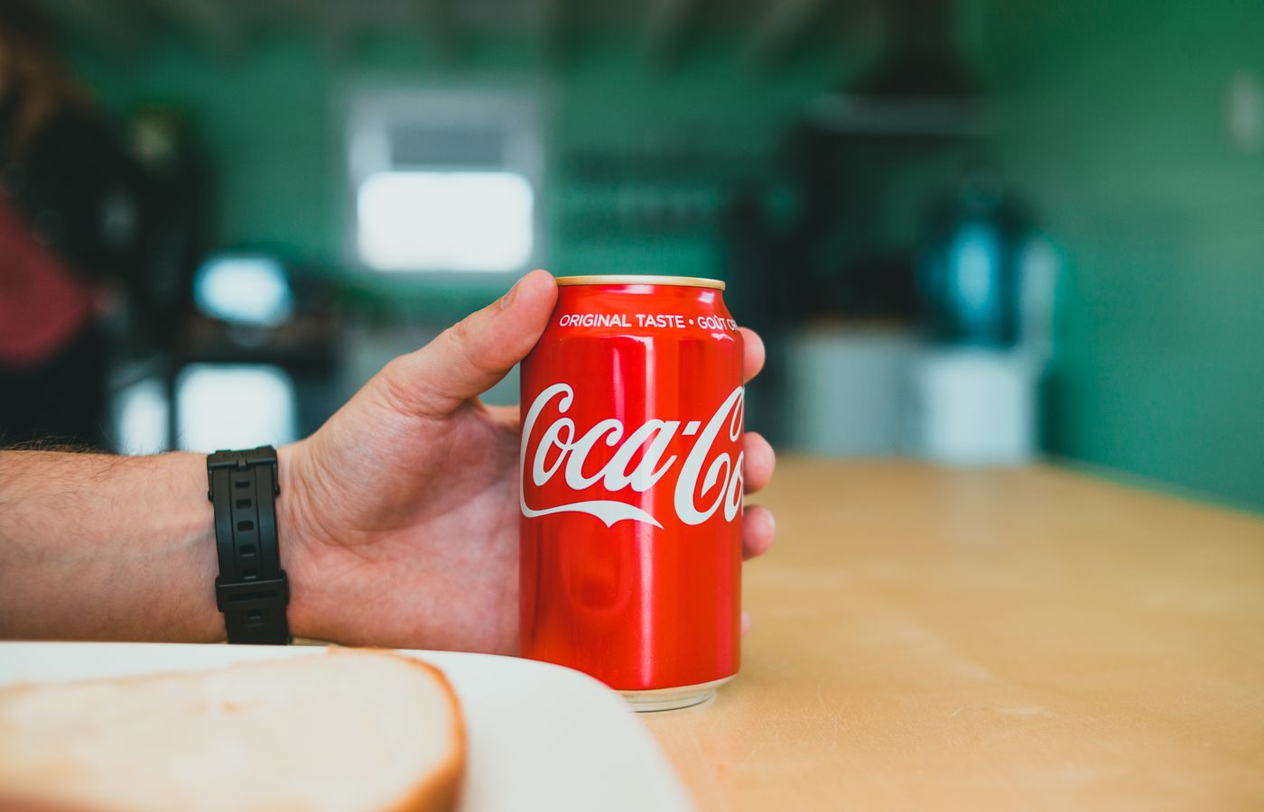 A person holding a red Coca-Cola can on a wooden table indoors.