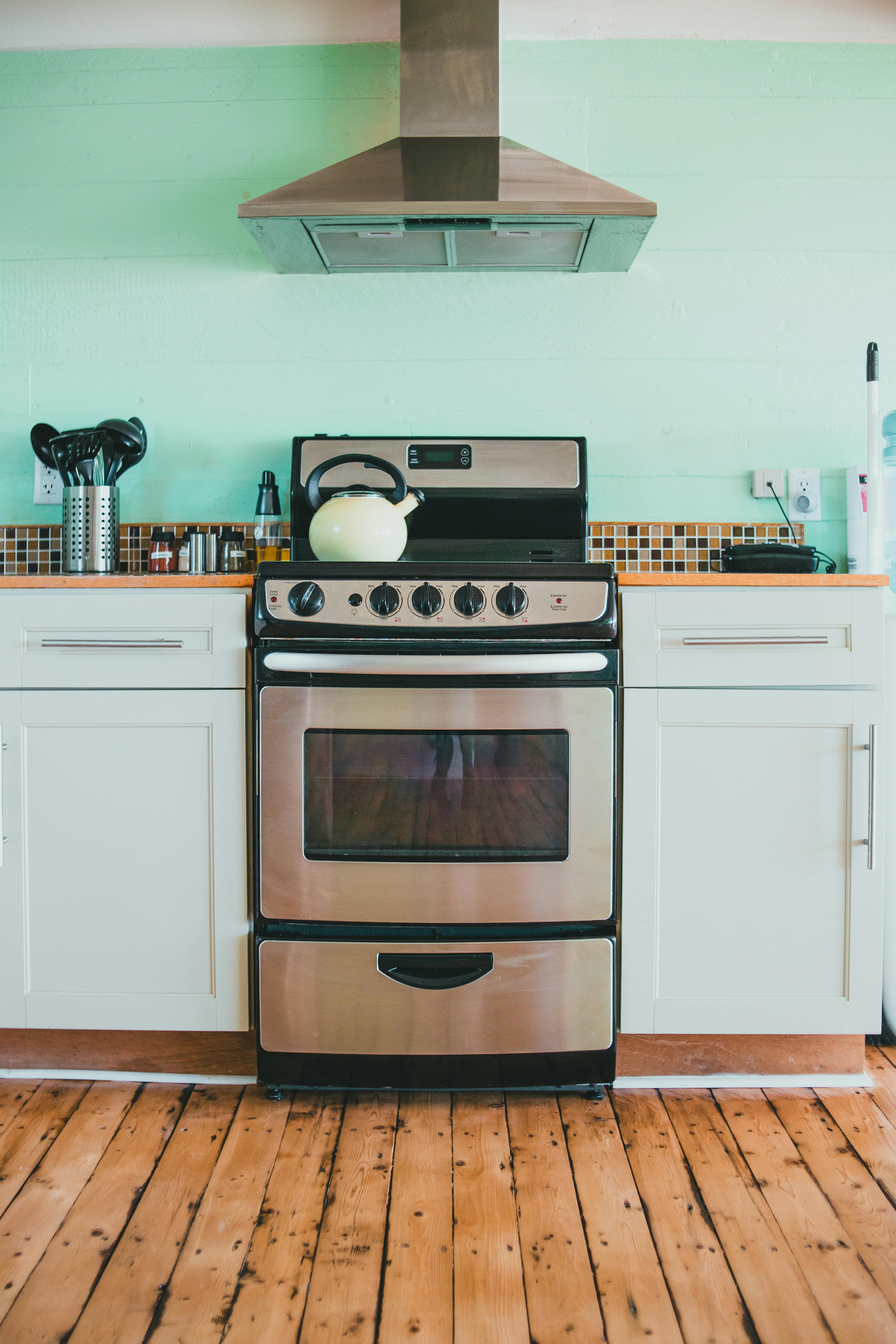 Kitchen with stainless steel stove and range hood, white cabinets, light green wall, wooden floor.