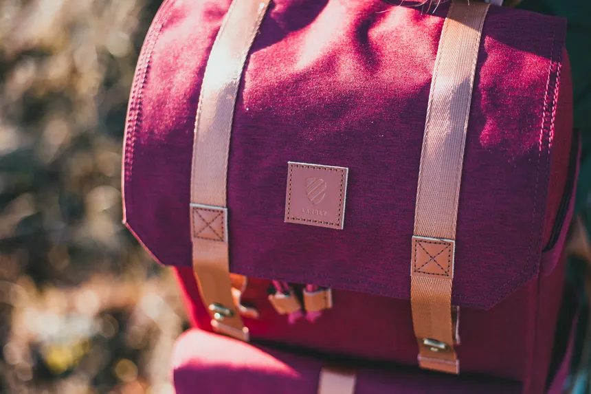 Explore the details of a stylish red backpack in an outdoor setting with natural lighting.
