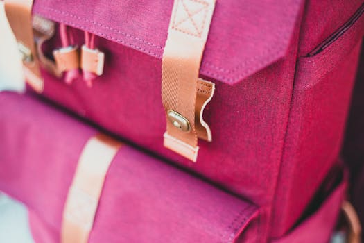 Detailed view of a red backpack featuring leather straps and metal clasps, ideal for travel.
