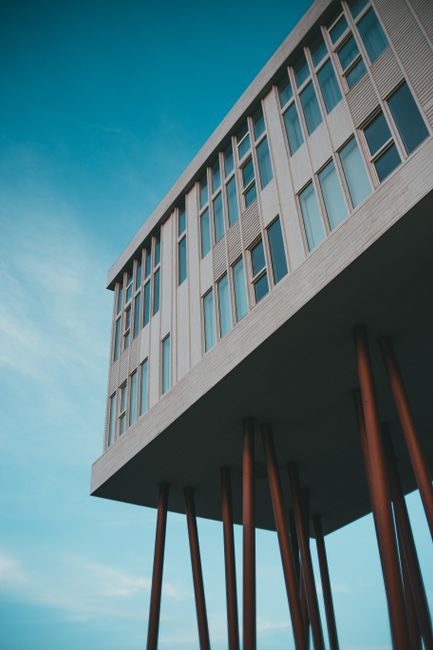 Low-angle shot of a contemporary building with stilts against a clear blue sky.