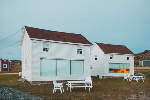 Two white cottages with red roofs and outdoor seating showcasing a serene village setting.