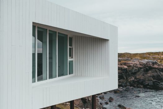 A minimalist modern building with large windows overlooking a rocky shoreline and ocean.