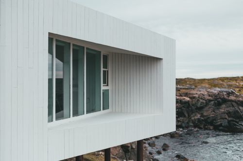 Free A minimalist modern building with large windows overlooking a rocky shoreline and ocean. Stock Photo