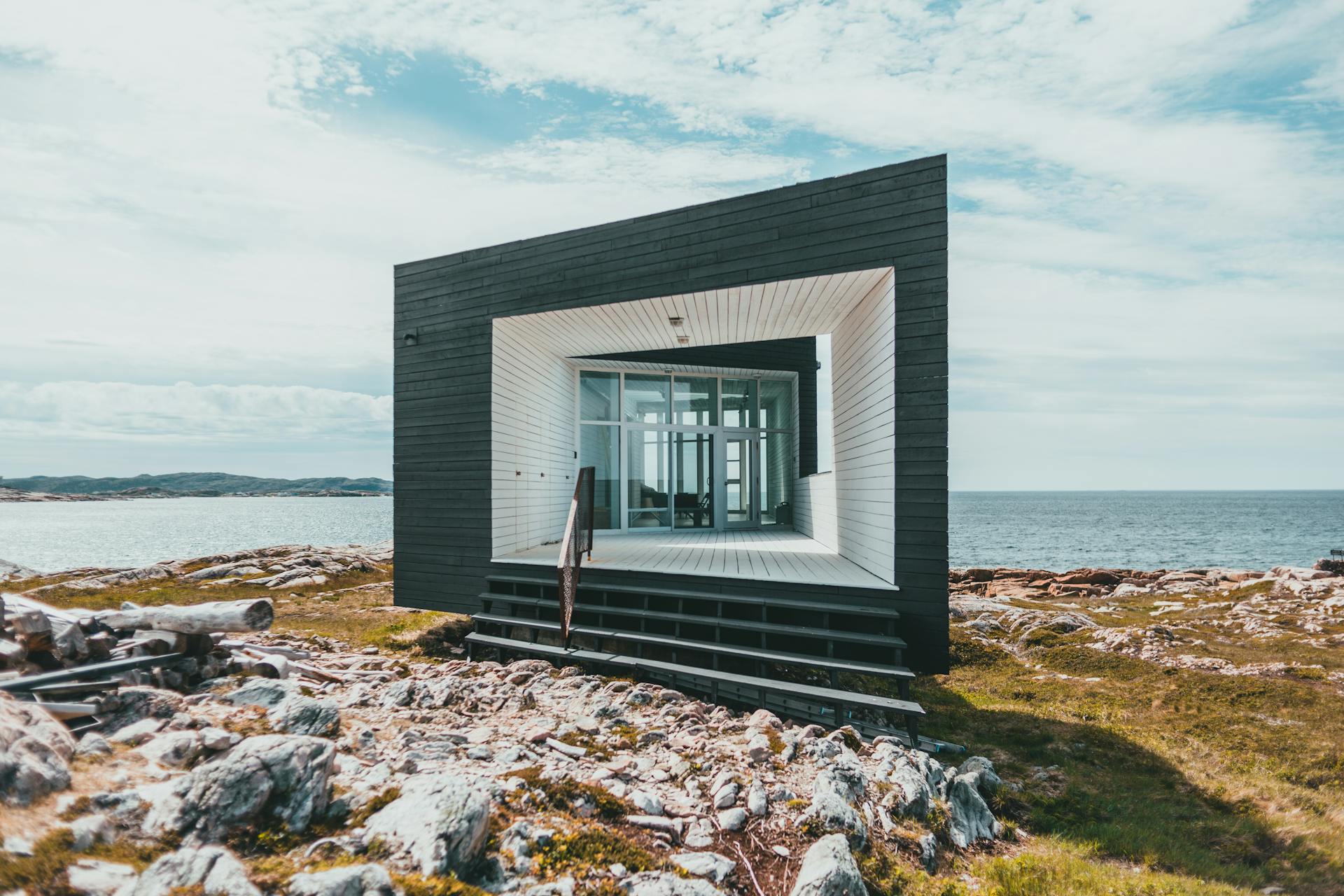 Contemporary tiny house on rocky coast with ocean view, showcasing minimalist architecture.