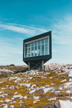A contemporary tiny house stands on a rocky terrain under a blue sky, showcasing modern design.