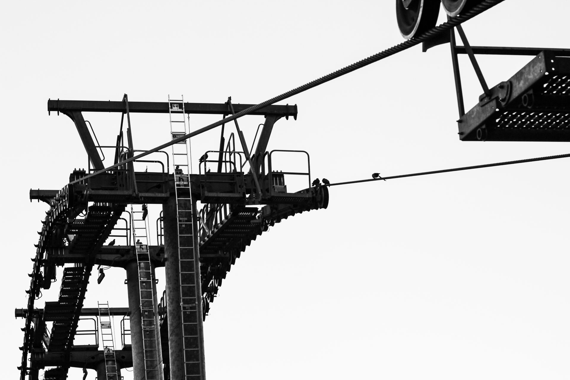 Black and white photo of an industrial cable system structure with ladders and steel machinery.