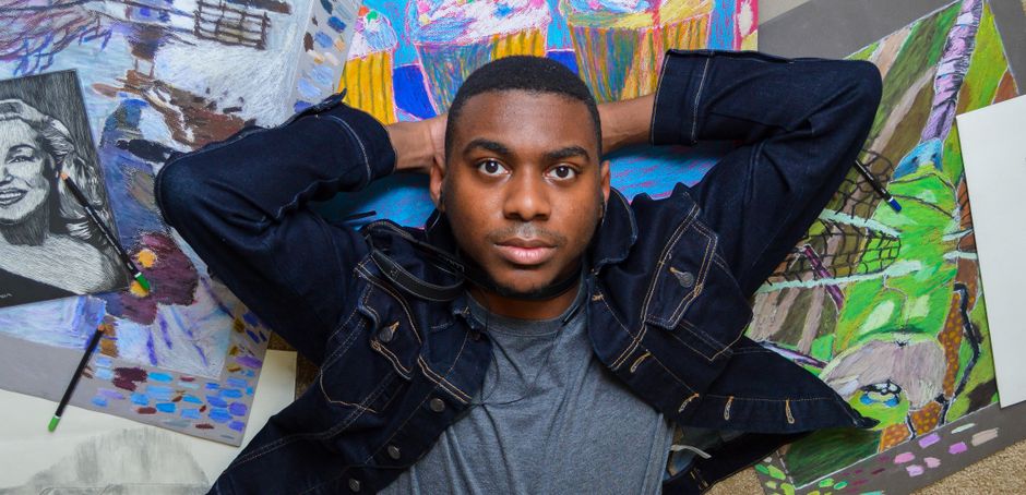 A young artist in a denim jacket lying surrounded by colorful paintings and sketches.