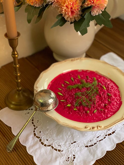 Plate of beetroot soup and ladle near flowers and candlestick