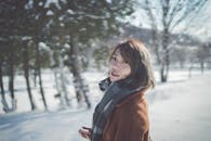在白雪皑皑的公园里，一位围着围巾、穿着棕色外套的女人微笑着