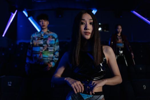 Fashionable young adults posing in a dimly lit, modern theater with neon lighting.