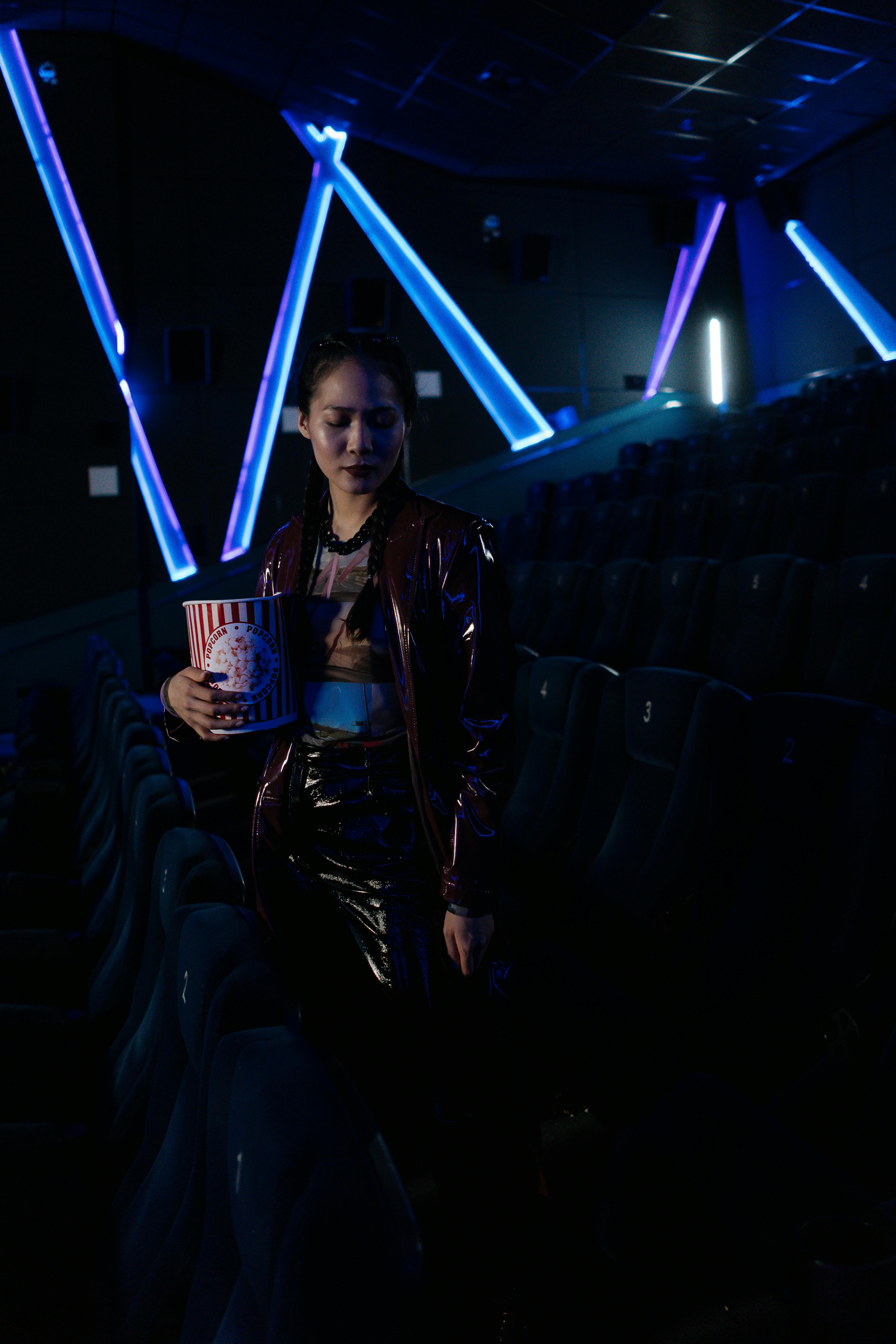 Free Asian woman holding popcorn in a modern cinema with neon lighting. Stock Photo
