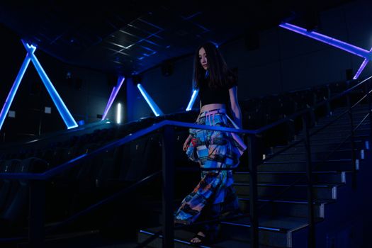 Stylish woman in vibrant outfit walking down stairs in a modern movie theater.