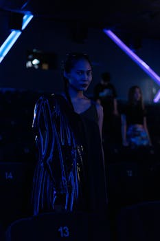 A fashionable Asian woman in a dark theater illuminated by neon lights.
