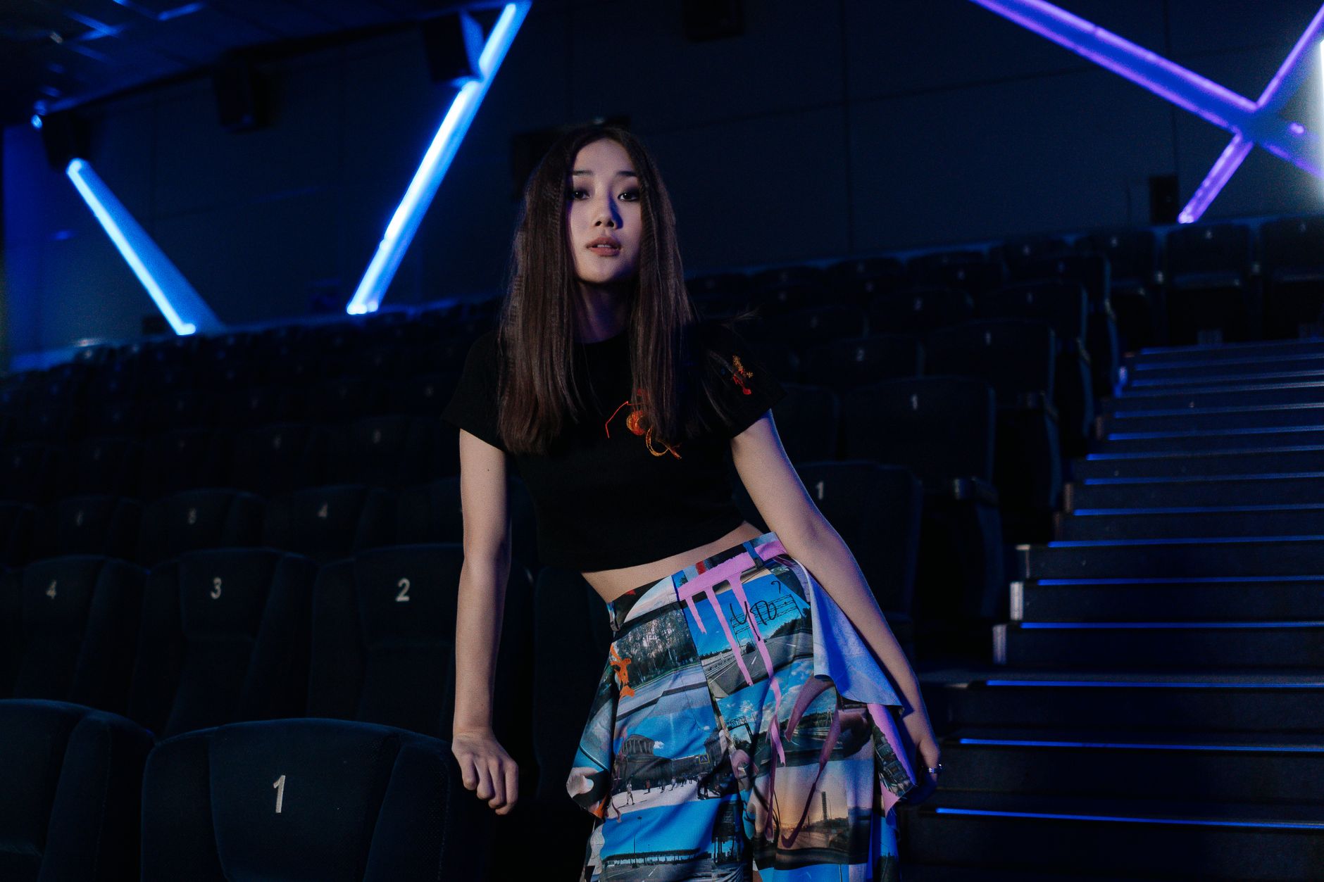 Fashionable woman posing in a modern, dimly lit movie theater interior.