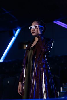 A woman in a shiny coat wearing 3D glasses in a dimly lit theater setting.