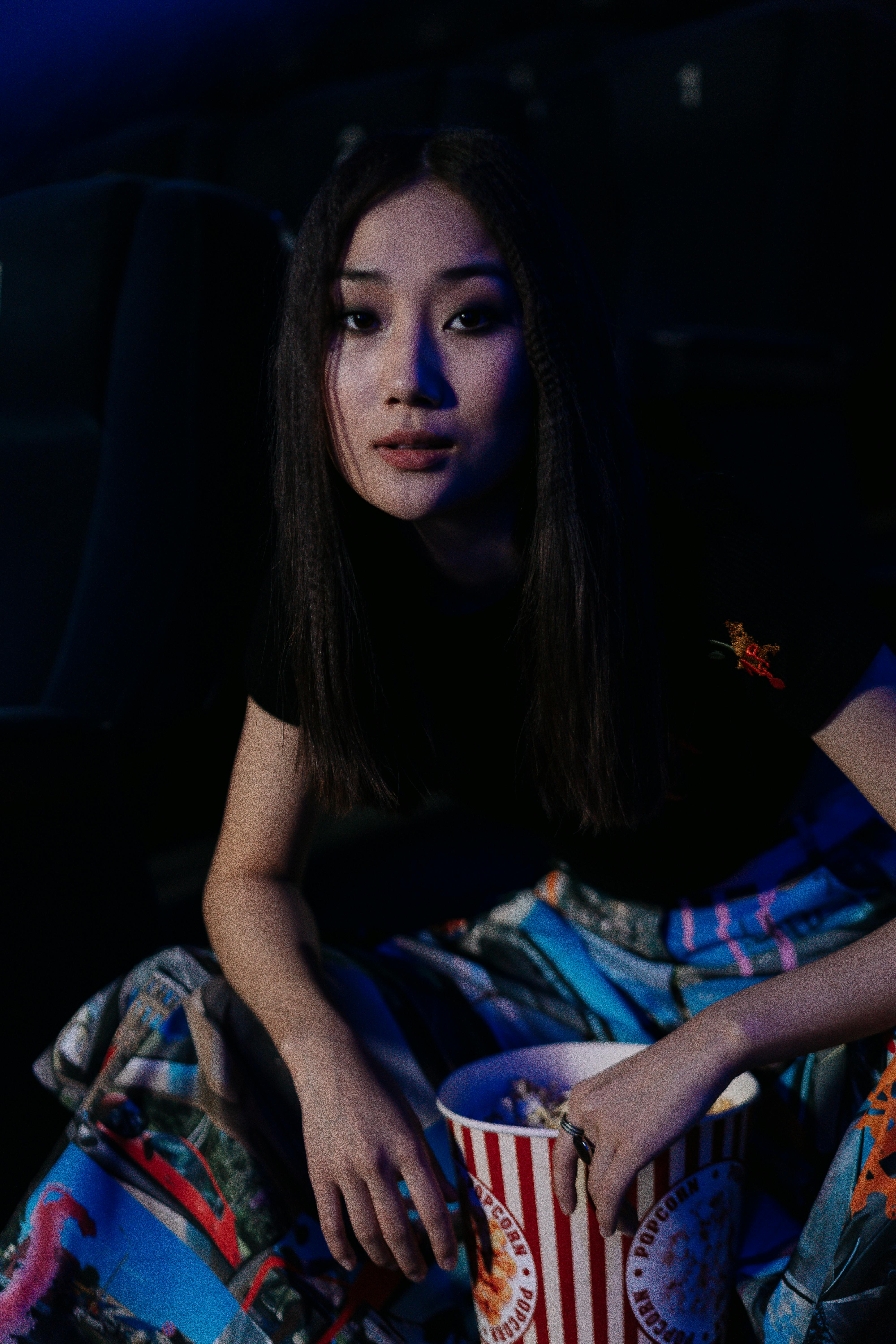 Free Young woman enjoying a movie indoors with stylish outfit and popcorn. Stock Photo