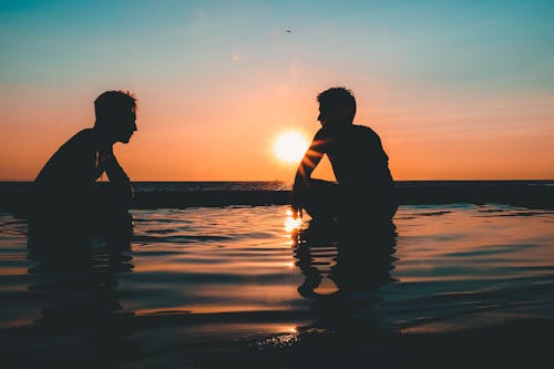 Фотография двух мужчин на берегу моря во время заката