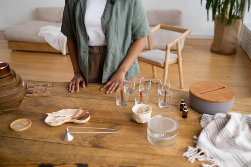 Free A craftswoman setting up her workspace for candle making, showcasing tools and materials on a wooden table. Stock Photo