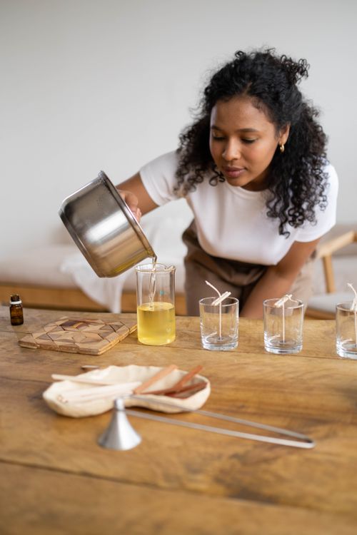 Free Black woman pouring hot wax for candle making, showcasing craft hobby indoors. Stock Photo