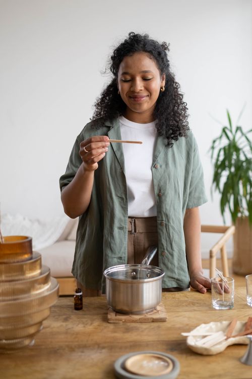 Free A woman enjoying candle making at home. She smiles as she holds a wick above a melting pot. Stock Photo
