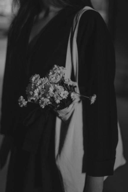 Artistic grayscale portrait of a woman with a shoulder bag and white flowers.