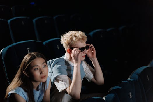 Couple seated in a theater watching a movie with empty seats around them.