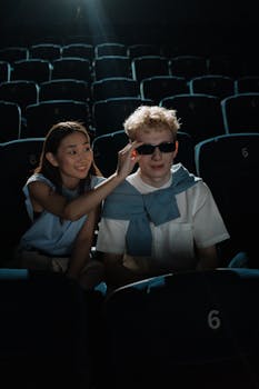 An interracial couple in a theater, sharing joyful moments while wearing sunglasses.