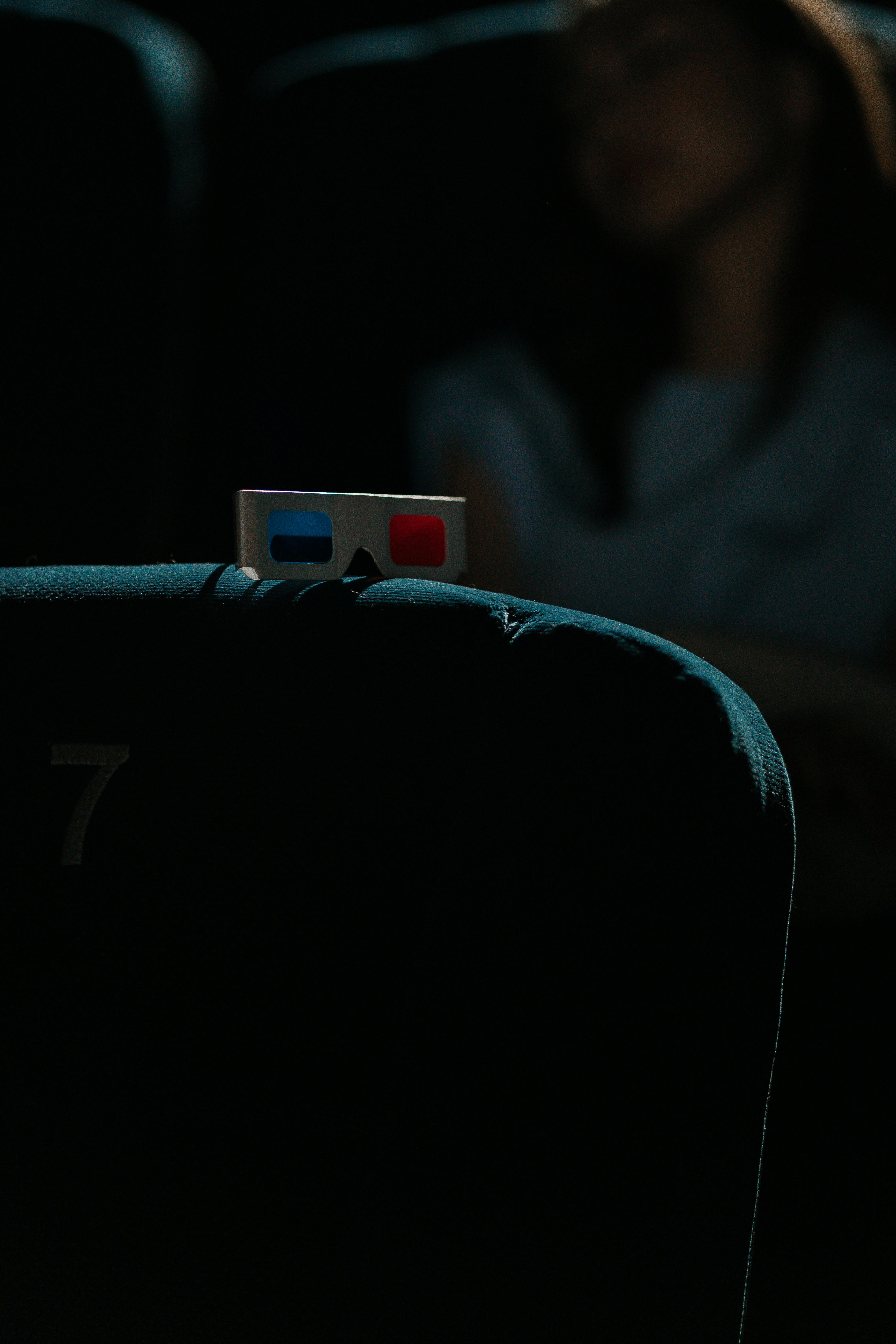 Free A dimly lit cinema featuring a pair of 3D glasses on a theater seat, capturing an immersive movie-going experience. Stock Photo