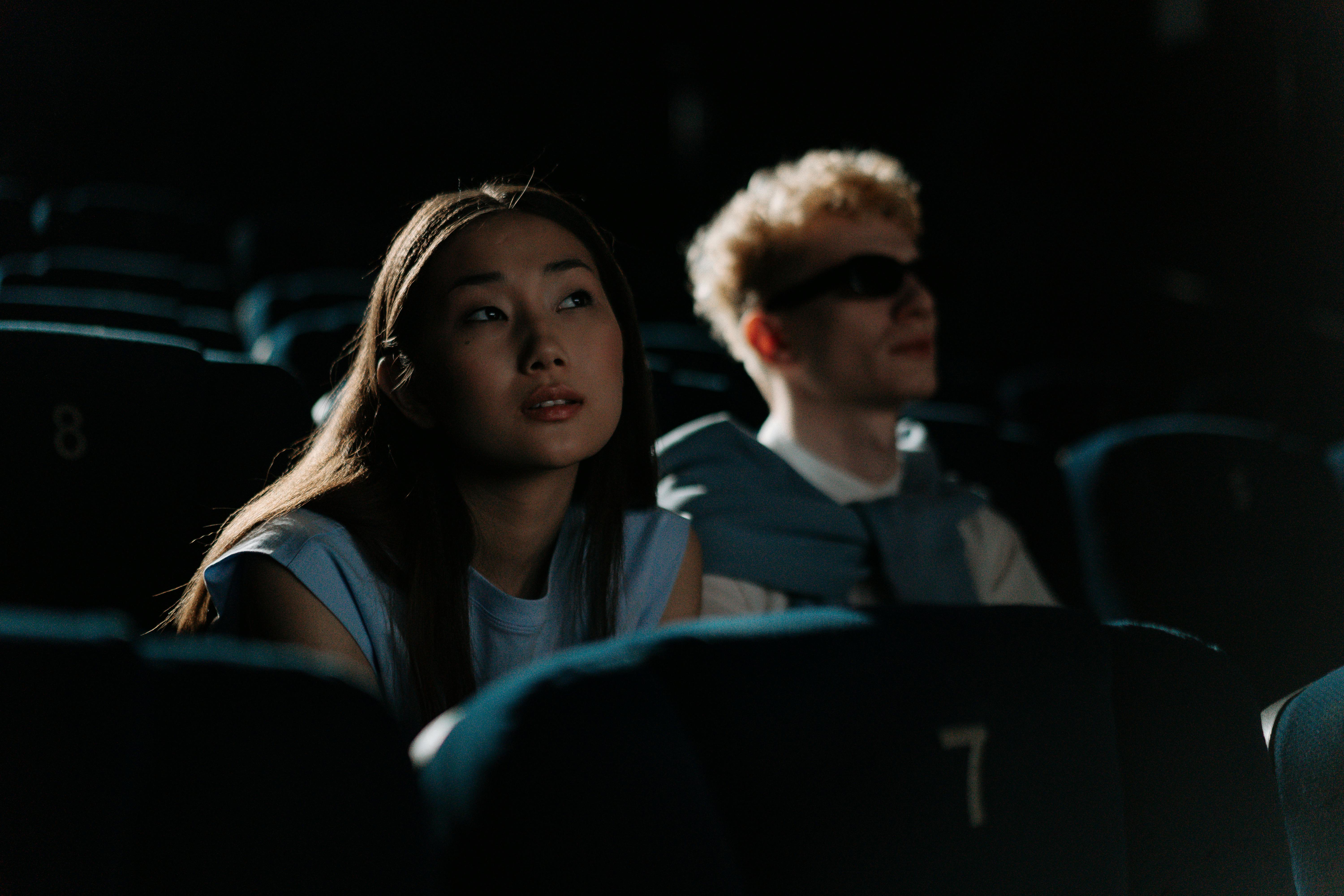Free Couple seated in a dimly lit movie theater enjoying a film together. Stock Photo