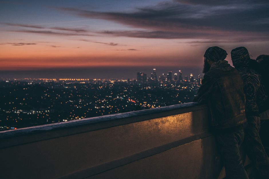 View of a city skyline at twilight from a balcony, with people silhouetted against the sunset.